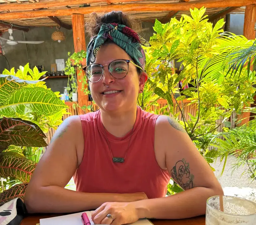 an image of Nicole, the tarot reader. She is sitting in a sunny cafe looking at the camera with a smile